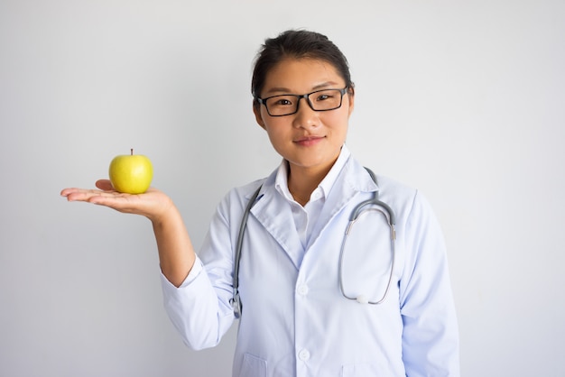 Zufriedene junge asiatische Ärztin, die Apfel auf Palme hält.