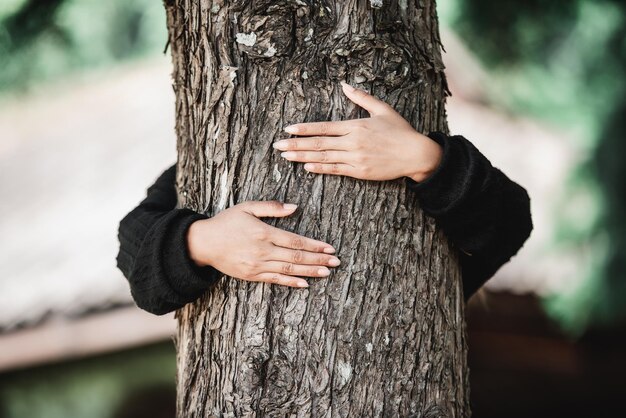Zufriedene junge Frau, die einen großen Baum mit einem glückseligen Ausdruck umarmt Konzept der Umweltpflege