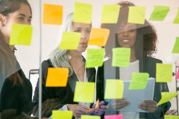 Zufriedene junge Geschäftsleute diskutieren Marketingplan und machen sich Notizen auf Aufklebern. Erfolgreiche selbstbewusste Kollegen in Anzügen treffen sich im Büroraum. Teamwork-, Business- und Brainstorming-Konzept