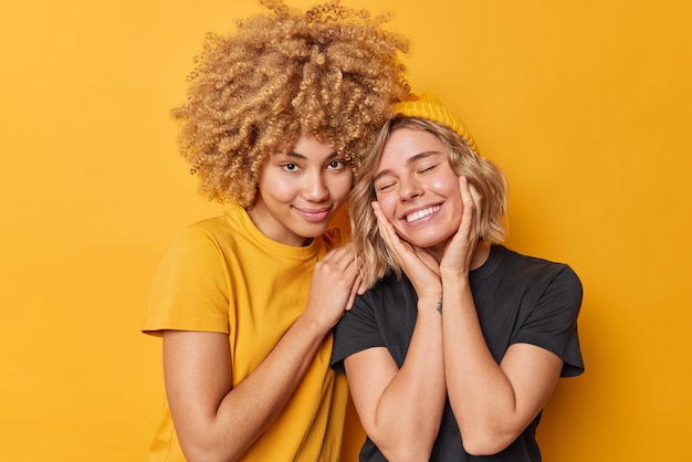 Zufriedene junge schöne Frauen fühlen sich froh, positive Emotionen auszudrücken, lächeln glücklich und stehen isoliert über lebhaftem gelbem Hintergrund eng beieinander Menschen Freundschafts- und Beziehungskonzept