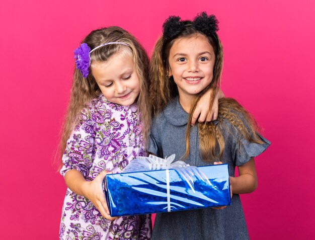 zufriedene kleine hübsche mädchen, die geschenkbox zusammenhalten, isoliert auf rosa wand mit kopierraum