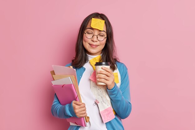 Zufriedene Managerin arbeitet mit Papierdokumenten hat Kaffeepause schließt Augen Haftnotiz mit gezeichneter Grafik auf der Stirn klebt trägt runde Brille.