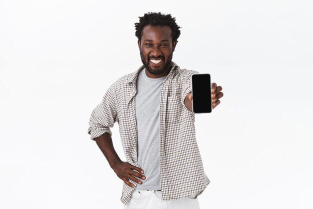 Zufriedener begeisterter junger afroamerikanischer lächelnder Mann, der Handybildschirm zeigt und Smartphone mit gezogener Hand hält