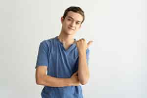 Kostenloses Foto zufriedener hübscher junger mann im blauen t-shirt beiseite zeigend