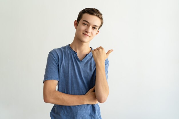 Zufriedener hübscher junger Mann im blauen T-Shirt beiseite zeigend