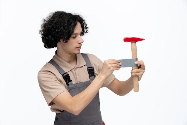 Zufriedener junger männlicher Bauarbeiter, der einen einheitlichen Klebebandhammer mit Klebeband isoliert auf weißem Hintergrund trägt