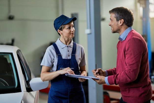 Zufriedener Kunde, der Dokumente unterzeichnet, während er mit einer Automechanikerin in einer Werkstatt kommuniziert. Der Fokus liegt auf der Frau