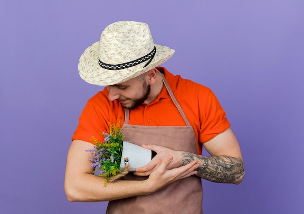 Zufriedener männlicher Gärtner mit Gartenhut hält und betrachtet Blumentopf