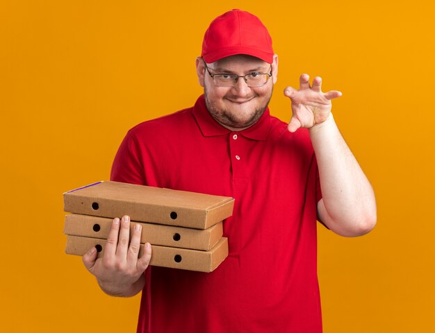 zufriedener übergewichtiger junger Lieferbote in optischer Brille, der Pizzakartons hält und Tigerpfote einzeln auf orangefarbener Wand mit Kopierraum gestikuliert