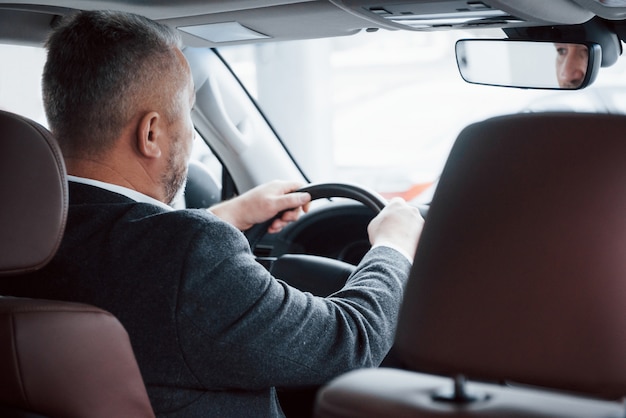 Zum Treffen gehen. Blick von hinten auf einen älteren Geschäftsmann in offizieller Kleidung, der ein modernes neues Auto fährt