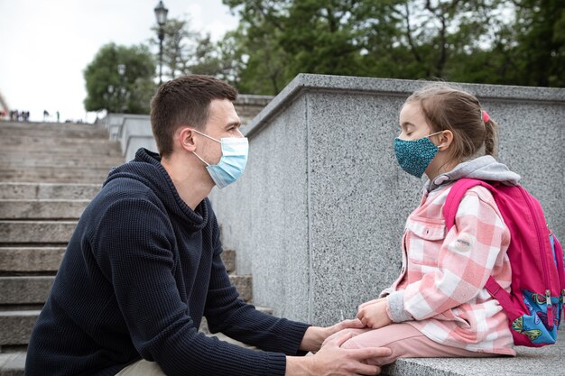 Zurück in die Schule, Pandemie. Junger Vater und kleine Tochter in einer Maske. Freundliche familiäre Beziehungen.