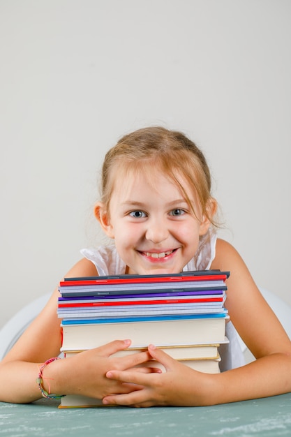 Zurück zum Schulkonzept auf Gips- und grauer Wandseitenansicht. kleines Mädchen, das Hefte und Bücher umarmt.