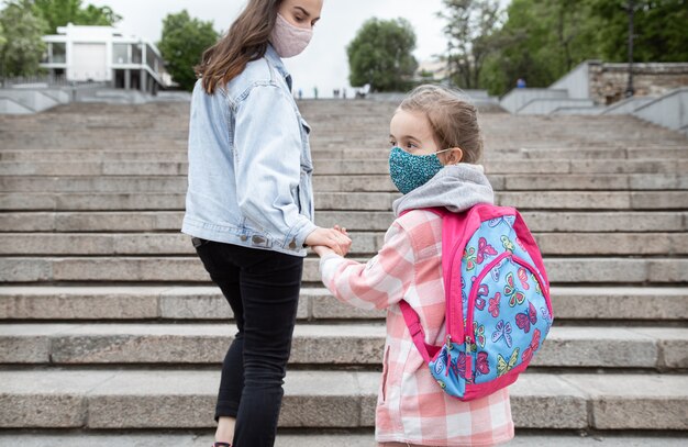Zurück zur Schule. Kinder mit Coronavirus-Pandemie gehen in Masken zur Schule. Mutter Händchen haltend mit ihrem Kind