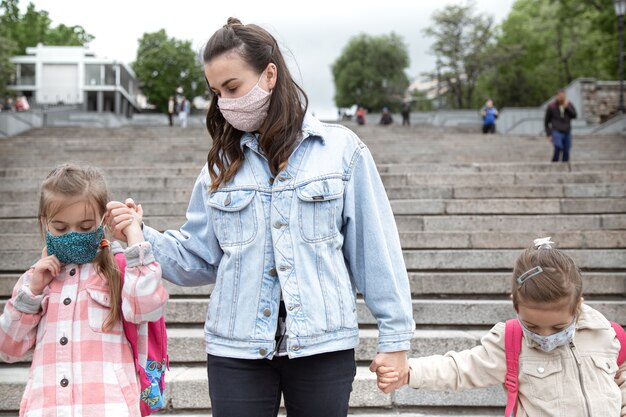 Zurück zur Schule. Kinder mit Coronavirus-Pandemie gehen in Masken zur Schule. Mutter Händchen haltend mit ihren Kindern.