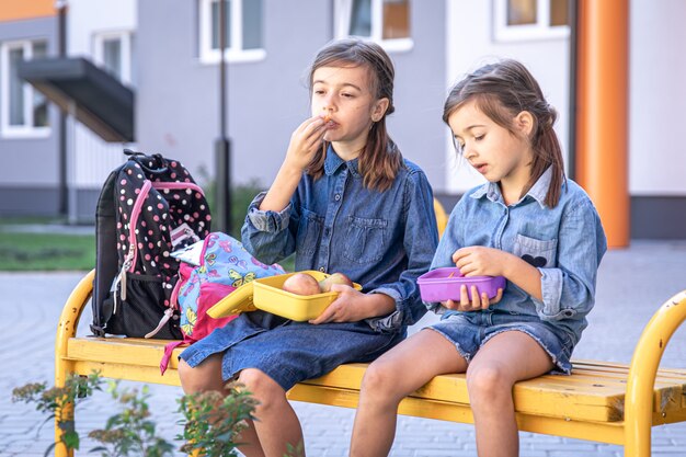 Zurück zur Schule. Nette kleine Schulmädchen, die auf der Bank im Schulhof sitzen und im Freien zu Mittag essen.