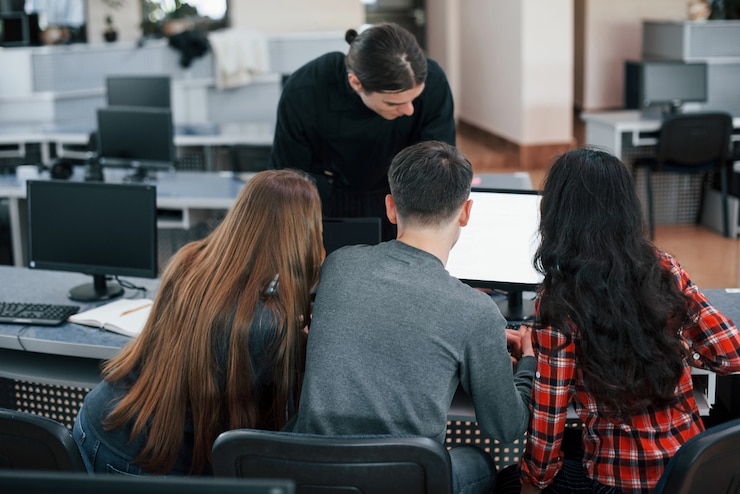Kostenlose Foto zusammen in der nähe eines monitors. gruppe junger leute in freizeitkleidung, die im modernen büro arbeiten