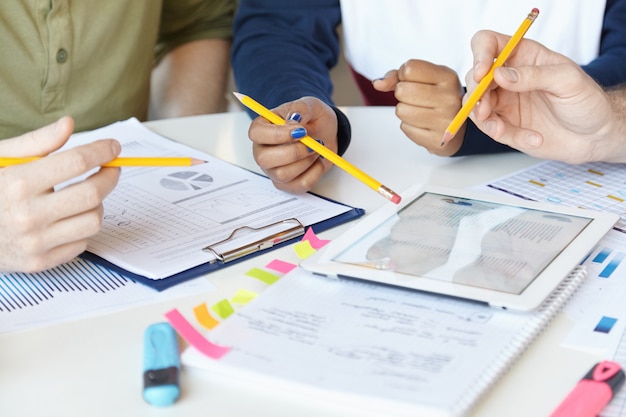 Zusammenarbeit. Gruppe von Marketingexperten, die gemeinsam an einem Startup-Projekt arbeiten und mit Blatt Papier und digitalem Tablet am Tisch sitzen.