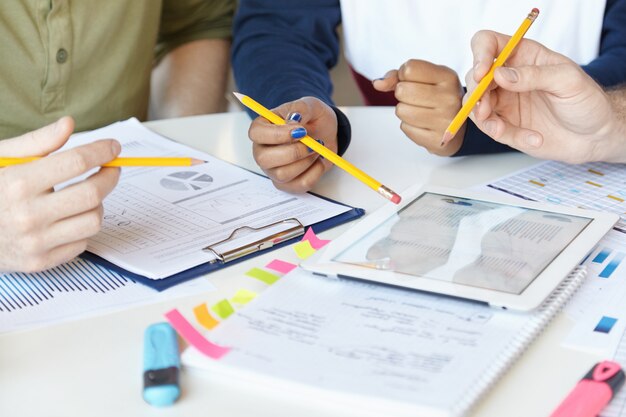 Zusammenarbeit. Gruppe von Marketingexperten, die gemeinsam an einem Startup-Projekt arbeiten und mit Blatt Papier und digitalem Tablet am Tisch sitzen.