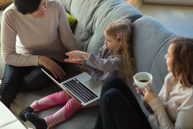 Zusammengehörigkeit. Glückliche liebevolle Familie. Großmutter, Mutter und Tochter verbringen Zeit miteinander. Kino schauen, Laptop benutzen, lachen. Muttertag, Feier, Wochenende, Urlaub und Kindheitskonzept.