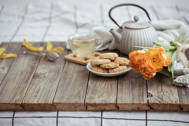Zusammensetzung mit einer Tasse Tee, einer Teekanne, Keksen und einem Strauß Tulpen