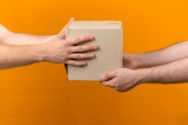 Zusteller, der Kastenpaket zum Kunden auf isolierter orange Seitenansicht gibt