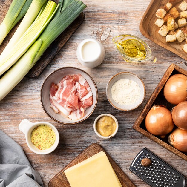 Zutaten für Lauch-Käsesuppe mit Croutons und Speck auf einem Holztisch Käse Zwiebel Lauch Olivenöl Speck Knoblauch Senf geriebener Cheddar Muskatnuss