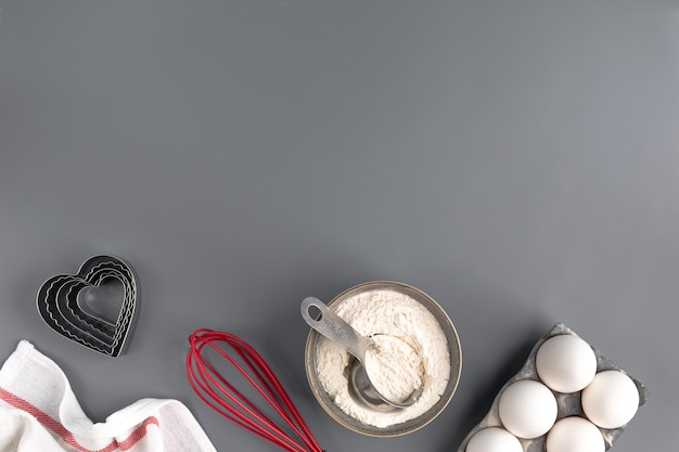 Zutaten zum Backen auf dunkelgrauem Hintergrund Mehl Eier Butter Herzform Schneebesen Textilien