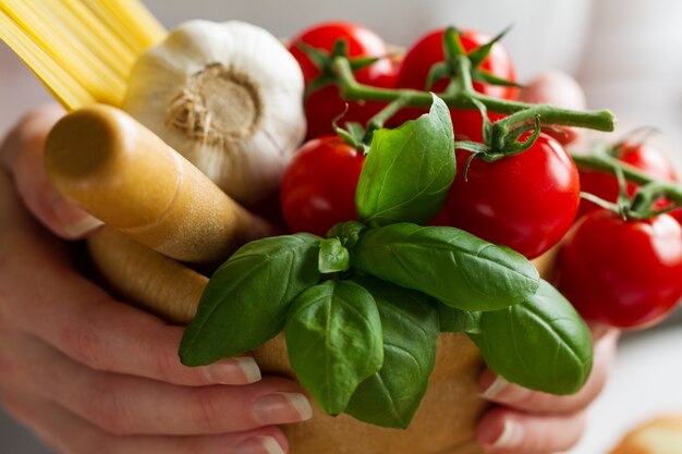 Zutaten zum Kochen von Nudeln. Tomaten, frischen Basilikum, Knoblauch, Spaghetti. Koch hält frische Zutaten zum Kochen. Nahansicht.