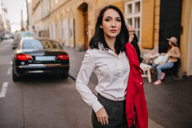 Zuversichtlich Frau mit den schwarzen Haaren, die auf der Straße mit Auto an der Wand aufwerfen