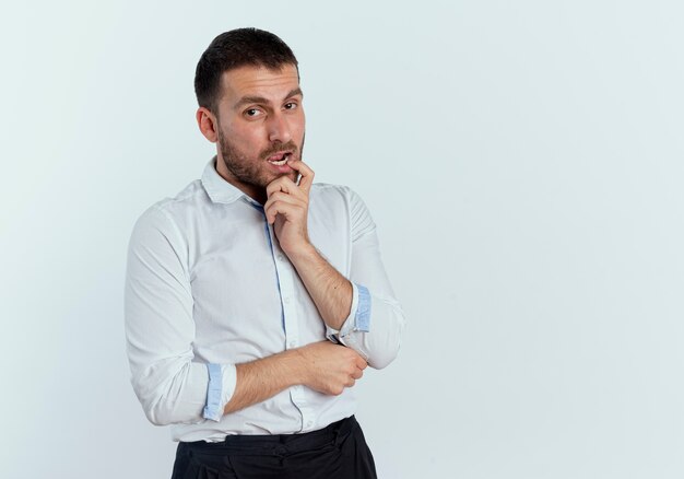 Zuversichtlich gutaussehender Mann legt Finger auf Mund, der auf weißer Wand isoliert schaut