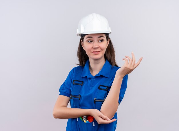 Zuversichtlich junge Baumeisterin mit weißem Schutzhelm und blauer Uniform hält Hand auf lokalisiertem weißem Hintergrund mit Kopienraum