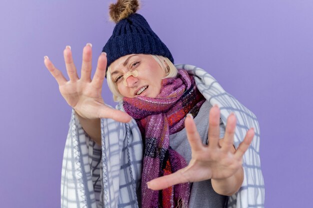 Zuversichtlich junge blonde kranke slawische Frau mit medizinischem Pflaster auf Nase, die Wintermütze und Schal trägt