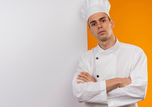 Zuversichtlich junge männliche coole tragende Kochuniform, die Hände mit weißer Wand auf isolierter gelber Wand mit Kopienraum kreuzt