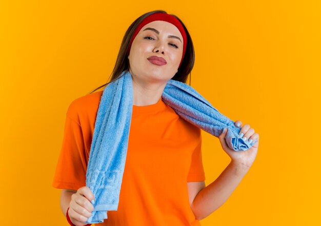 Zuversichtlich junge sportliche Frau, die Stirnband und Armbänder mit Handtuch um den Hals hält Handtuch suchen