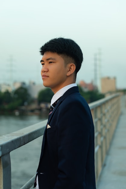 Zuversichtlich junger asiatischer Mann in einem Anzug, der auf einer Brücke steht wegschaut