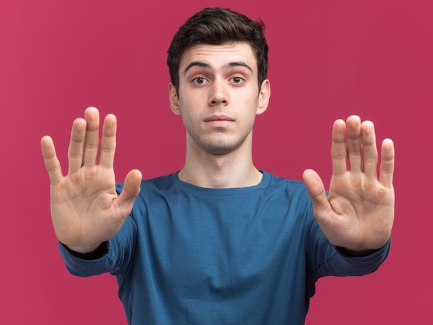 Zuversichtlich junger brünetter kaukasischer Junge, der Stoppschild mit zwei Händen auf rosa gestikuliert