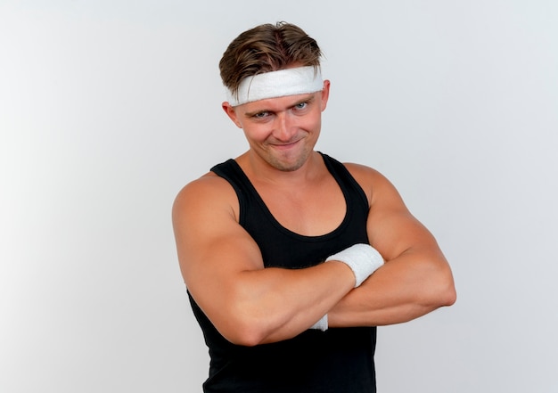 Zuversichtlich junger hübscher sportlicher Mann, der Stirnband und Armbänder trägt, die mit geschlossener Haltung stehen, lokalisiert auf Weiß mit Kopienraum