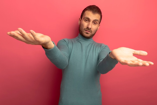 Zuversichtlich junger kaukasischer Mann, der leere Hände lokalisiert auf purpurroter Wand zeigt
