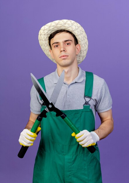 Zuversichtlich junger männlicher Gärtner, der Gartenhut und Handschuhe trägt, hält Haarschneidemaschine