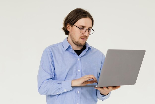Zuversichtlich junger schöner Mann im Hemd, das Laptop hält und lächelt, während gegen weißen Hintergrund stehend