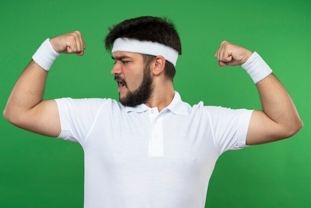 Zuversichtlich junger sportlicher Mann, der Stirnband und Armband trägt, zeigt starke Geste lokalisiert auf Grün