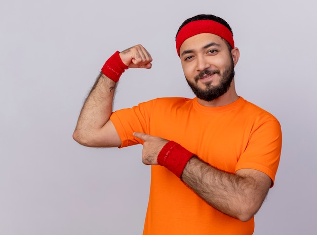 Zuversichtlich junger sportlicher Mann, der Stirnband und Armband zeigt, zeigt starke Geste lokalisiert auf weißem Hintergrund