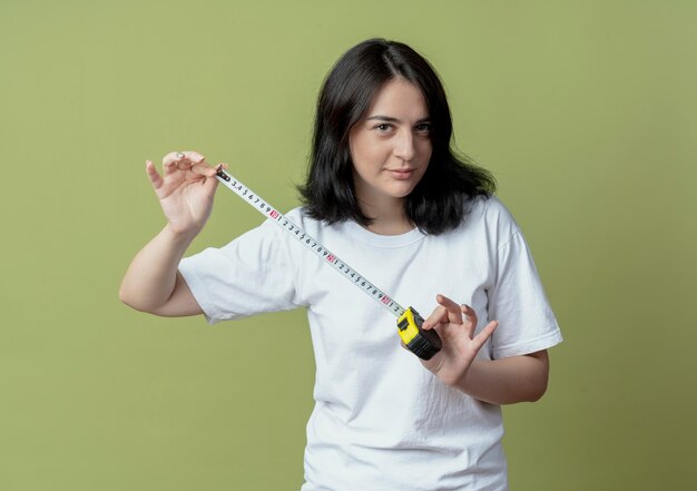 Zuversichtlich junges hübsches kaukasisches Mädchen, das Bandmeter lokalisiert auf olivgrünem Hintergrund hält