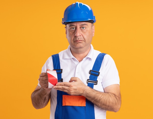 Zuversichtlich kaukasischer erwachsener Baumeister Mann in Uniform hält Klebeband auf Orange