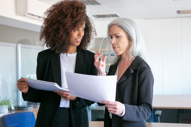 Zuversichtlich Partnerinnen diskutieren Dokument im Büroraum. Zwei attraktive, erfolgreich fokussierte Geschäftsfrauen, die Dokumentation studieren, berichten gemeinsam. Teamwork-, Geschäfts- und Managementkonzept