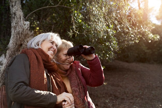 Zwei ältere Freundinnen, die eine Wanderung in der Natur genießen, während sie ein Fernglas benutzen
