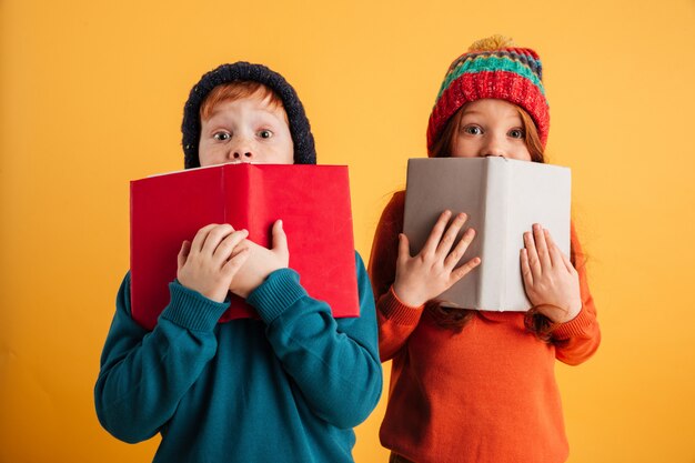 Zwei ängstliche kleine rothaarige Kinder, die Gesichter mit Büchern bedecken.