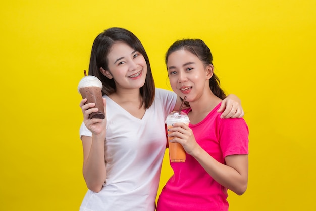 Zwei asiatische Frauen, die gefrorenen Milchtee und gefrorenen Kakao auf einem Gelb trinken.