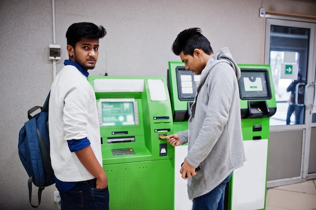 Zwei asiatische Männer ziehen Bargeld von einem grünen Geldautomaten ab