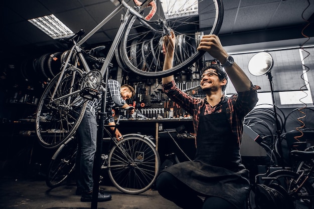Zwei attraktive Handwerker reparieren in ihrer dunklen Werkstatt ein kaputtes Fahrrad.
